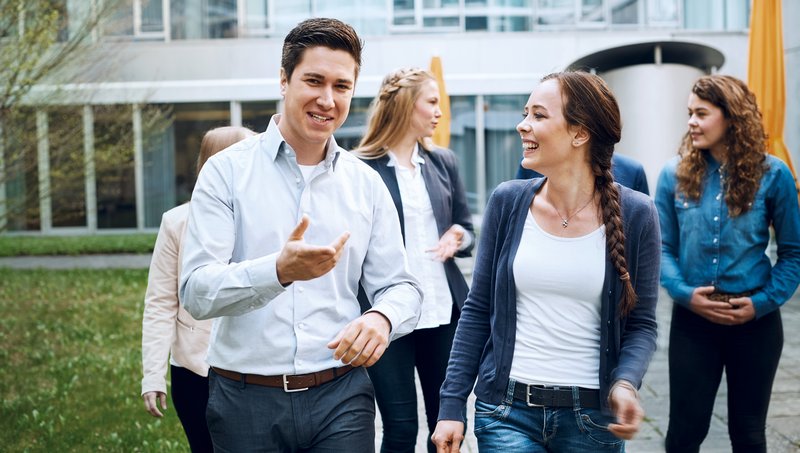 Eine Gruppe junger Menschen geht lächelnd durch einen Gebäudeinnenhof